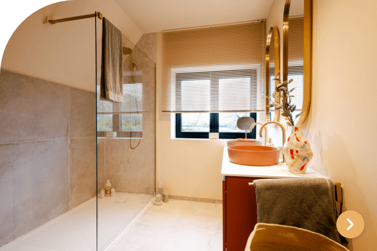 Warme badkamer met beige tegels, oranje wastafel en glazen douchewand